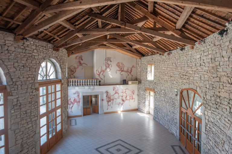 Stenen kerk met muurschilderingen van paarden, rustiek en elegant interieur, zichtbaar houten geraamte, warme sfeer, ideaal voor bruiloften of privé-evenementen, Château Yams.