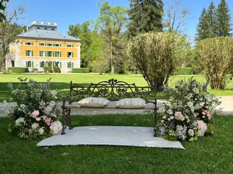 A wrought iron bench decorated with cushions and flowers for a wedding set in the splendid green gardens of the Villa Palladiana visible in the background.
